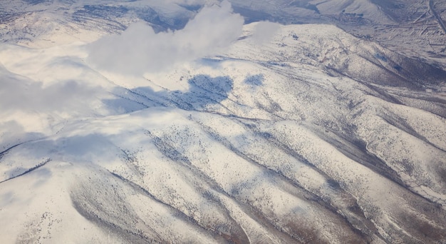 Snowy mountains background and white clouds above them Aerial photo from plane window