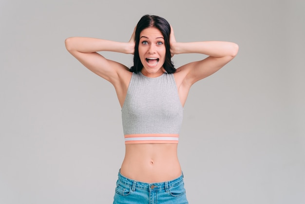 So excited! Surprised young woman keeping mouth open and holding head in hands while standing