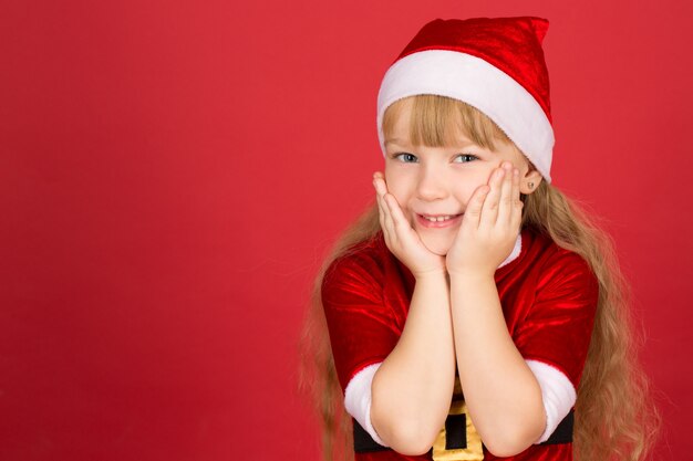 So many presents to come. Studio shot of a little girl wearing Christmas outfit cupping her face in her hands looking excited and smiling cheerfully