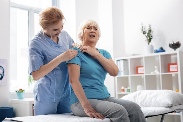 So strong. Emotional aged woman pointing at her shoulder while feeling pain there during the massage