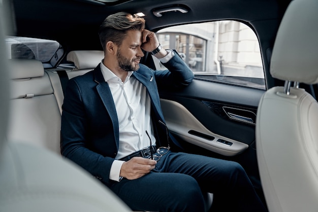 So tired. Frustrated young man in formalwear keeping eyes closed while sitting in the car