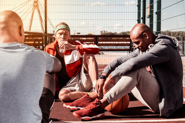 So tired. Pleasant good looking men sitting on the ground while resting together after the basketball match