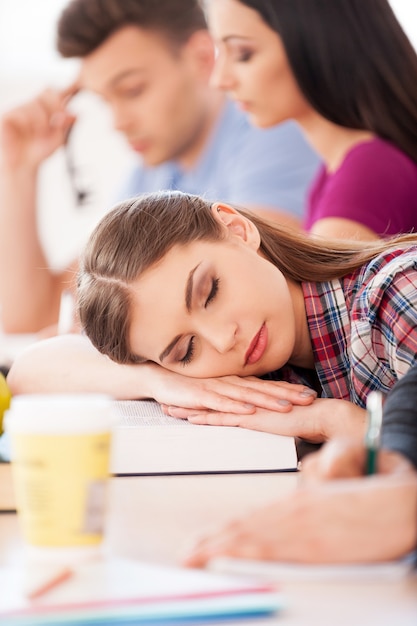 So tired of studying. Beautiful female student sleeping while sitting at the desk with other students