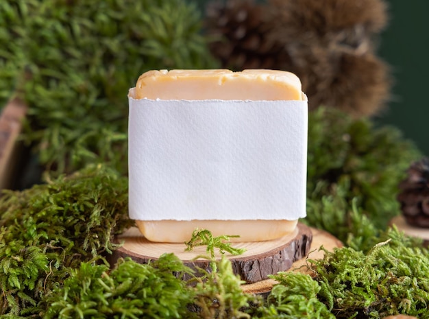 Soap bar with blank label on wooden piece near green moss close up Natural cosmetic mockup