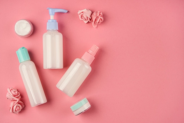 Soap and cream containers with small flowers on pink background