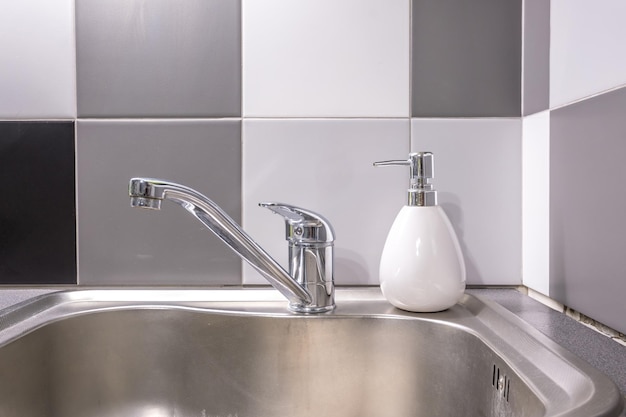 Soap and shampoo dispensers near Ceramic Water tap sink with faucet in expensive kitchen