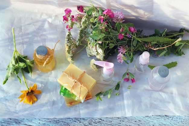 Soap, spray, bouquet of medicinal herbs and glass bottles with aromatic oil on a wooden table