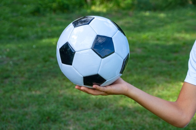 Soccer ball white and black leather in hand of football player on green grass