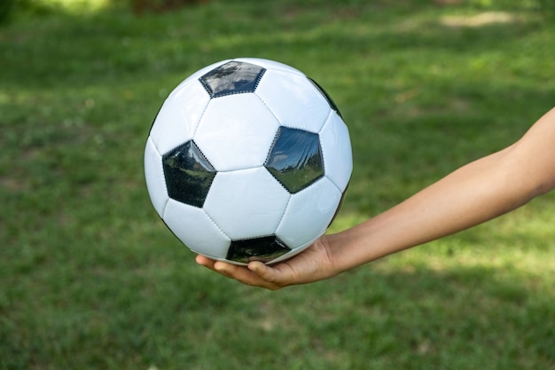 Soccer ball white and black leather in hand of football player on green grass