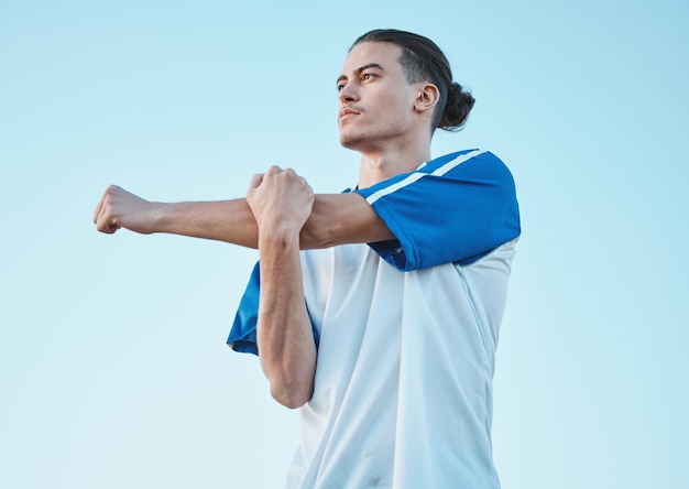 Soccer fitness and stretching with a man on a blue sky background in preparation of a game or competition Sports health and warm up with a young male athlete getting ready for training or practice