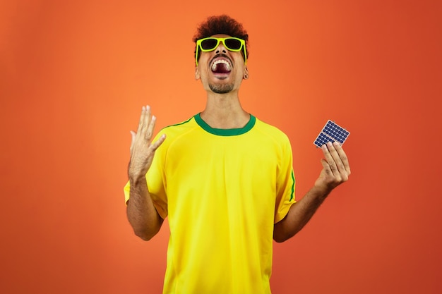 Soccer Player Black Man Celebrating Holding Solar Photovoltaic Panel Isolated on Orange Background