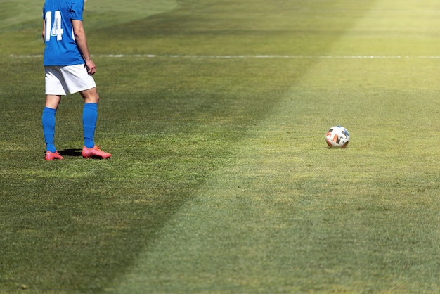 Soccer player ready to take a free kick a few meters away from the ball on a natural grass pitch