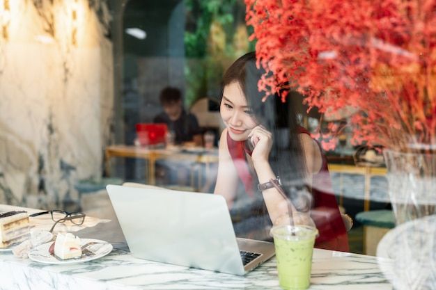 Social connection and lifestyle concept - woman smiling using smartphone and laptop in coffee shop