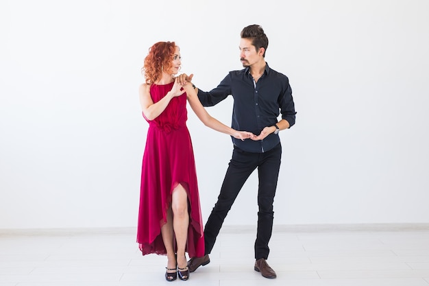 Social dance, bachata, kizomba, salsa, tango concept - Woman dressed in red dress and man in a black costume over white wall.