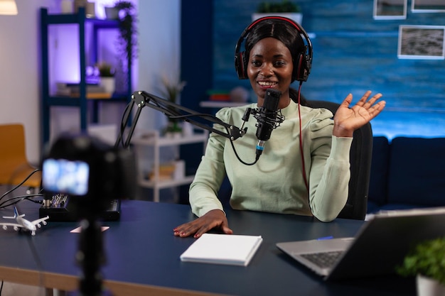 Social media woman creator greeting subscribers while recording video content for youtube channel. Influencer sitting in podcast studio filming tutorial using production equipment. On air talk show