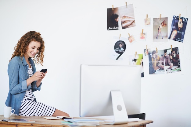 Social media in the workplace Shot of a young woman using a cellphone while sitting on her desk in an office