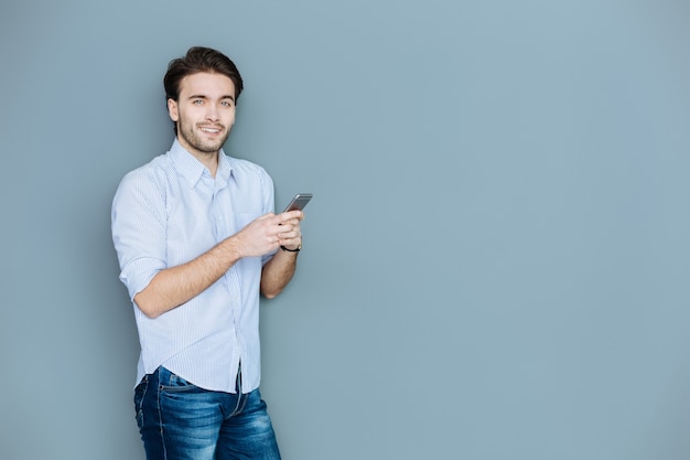 Social networking. Delighted positive young man holding his smartphone and using it while chatting on social network