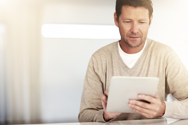 Social networking mature and man with tablet and at table at his home Blog or internet connectivity technology and mockup space with male person reading an email or report at desk his house