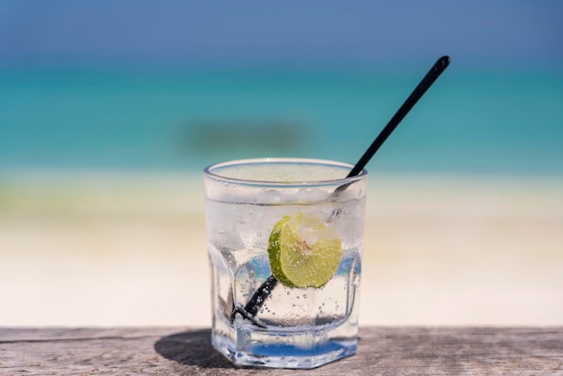 Soda water with lime and ice on a wooden table near the sea on the beach