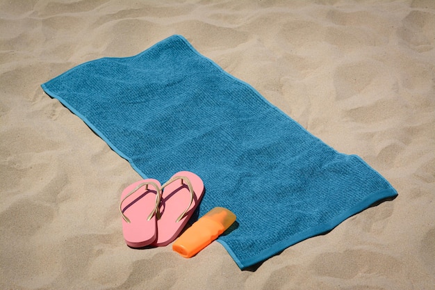 Soft blue beach towel pink flip flops and sunscreen on sand Space for text