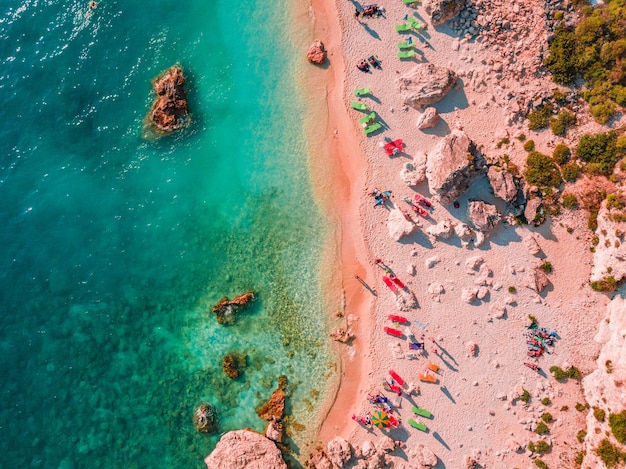 Soft blue waves of the sea with white foam on tropical sandy beach with rocks toned trendy living coral color of year 2019 shoot from drone.