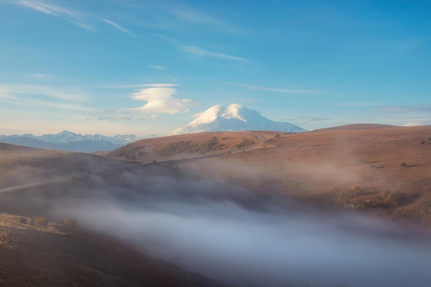 Soft focus Elbrus Mountain in a dense morning fog and sunny slope Mystical landscape with beautiful snowy rocks in low clouds Beautiful mountain foggy scenery