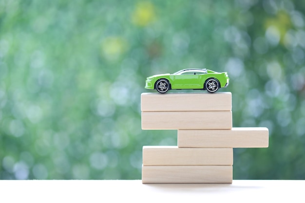 Soft focus of miniature car model on wooden block on natural green background