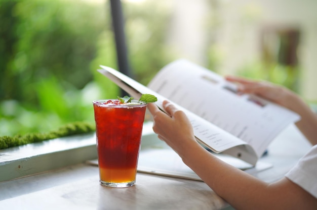 Soft focus and selective focus glass of ice honey lemon tea on table with blurred hand holding book.