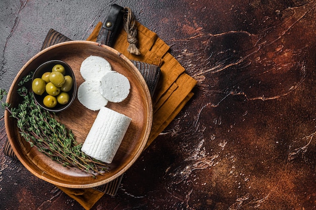 Soft Goat cheese chevre in a plate with thyme and olives Dark background Top view Copy space