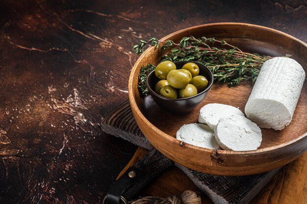 Soft Goat cheese chevre in a plate with thyme and olives Dark background Top view Copy space