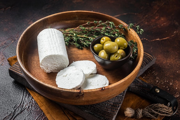 Soft Goat cheese chevre in a plate with thyme and olives Dark background Top view