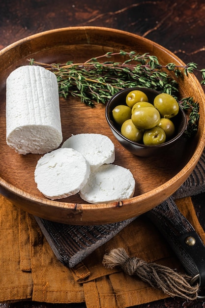 Soft Goat cheese chevre in a plate with thyme and olives Dark background Top view