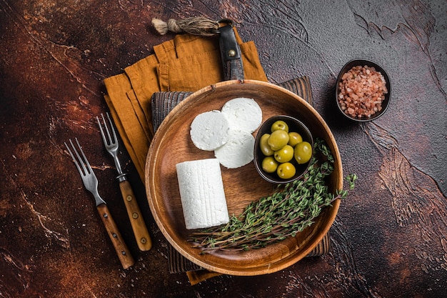 Soft Goat cheese chevre in a plate with thyme and olives Dark background Top view