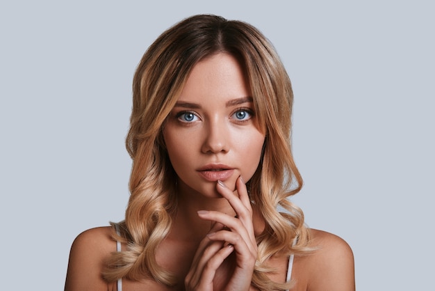 Soft sensuality. Beautiful young woman looking at camera while standing against grey background