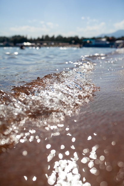 A soft wave runs on a sandy shore on a summer day. Empty space can be used as background