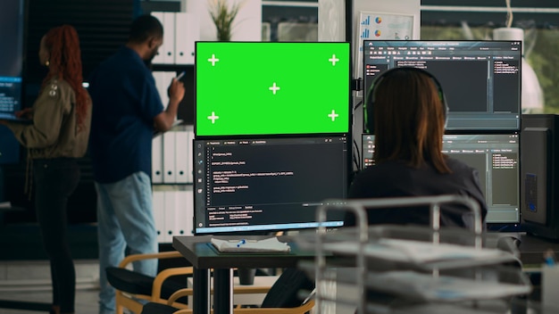 Software developer analyzing greenscreen and server code on multiple monitors in busy ai developing agency. Looking at isolated copyspace with chromakey display and mockup template.