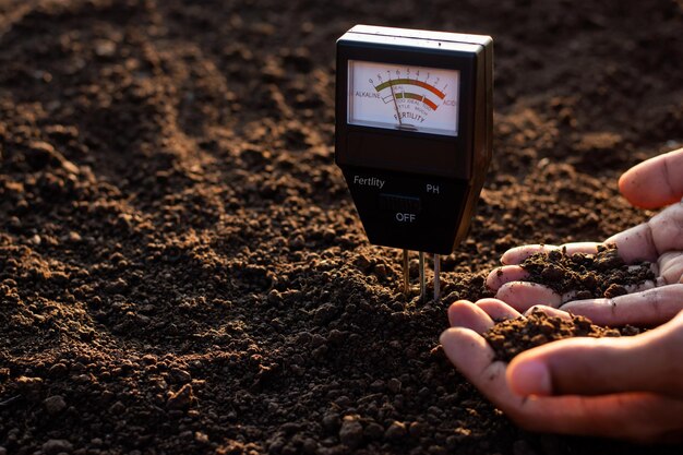 Photo a soil meter and a farmer's hands are picking up soil for planting.