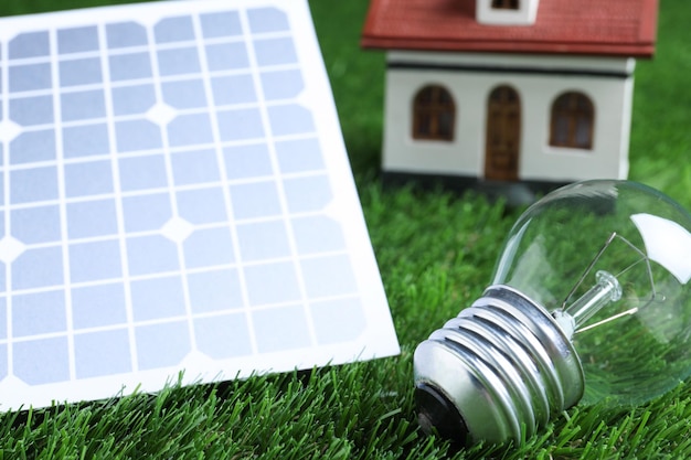 Solar panel light bulb and house model on green grass closeup