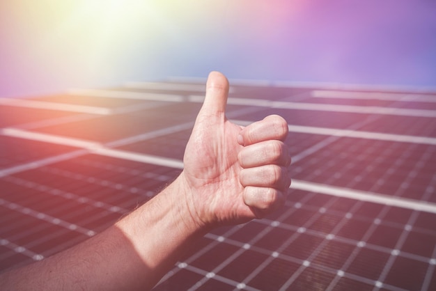 Solar panel on the roof produces electricity on the background of a hand with a finger up