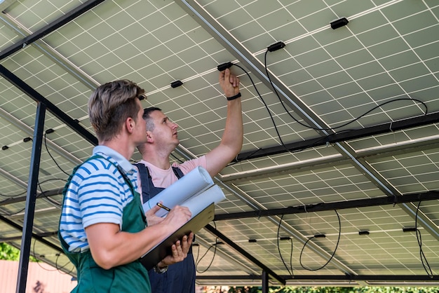 Below the solar panels two young workers in uniform stand and watch for any breakdowns