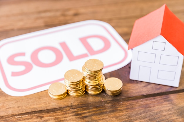 Sold tag with stacked coins and house on wooden desk