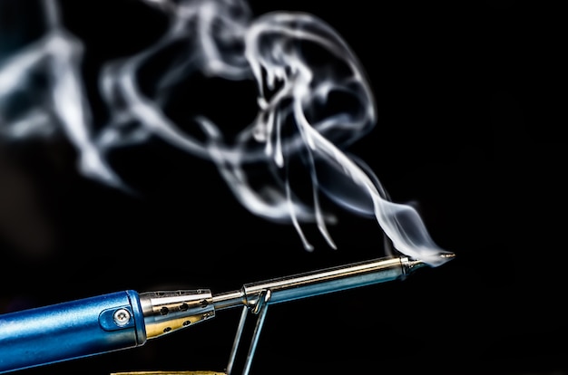 Soldering iron with smoke on a black background. Electrical, electronics