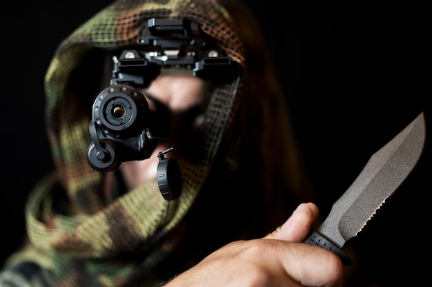 Photo a soldier in camouflage with a night vision device and a knife in his hand