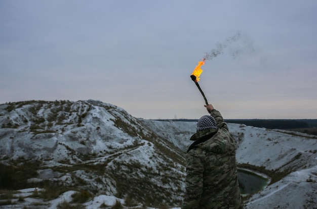 Soldier is holding torch with fire Man in camouflage uniform and checkered bandana Person in the mountains gorge White hills and dry grass in the desert