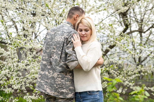 Soldier is hugging a woman outdoor. Reunion of a couple in the evening park.