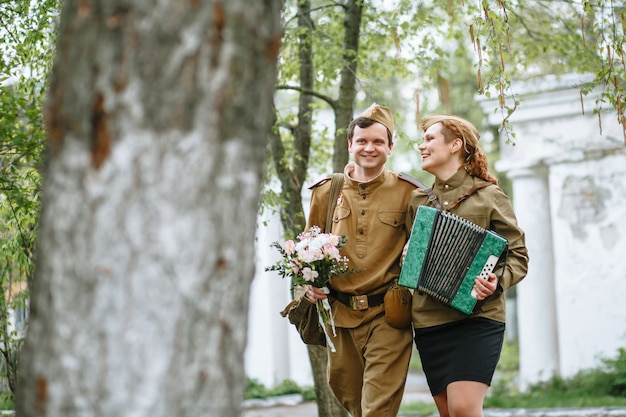 Soldier walks down the alley, hugging a military woman playing an accordion