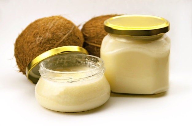 Photo solid homemade coconut oil in glass jar with metal gold lid and fresh coconuts on white  close up view. selective soft focus. . text copy space. coconut butter concept