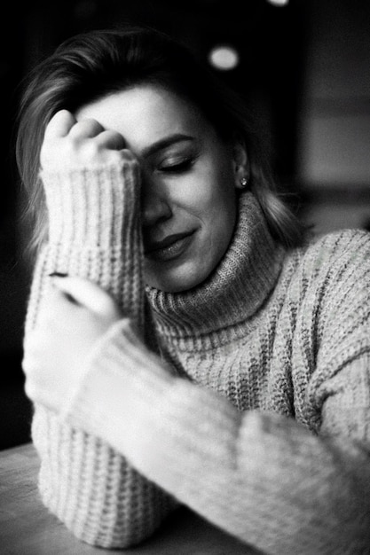 Photo a solitary moment captured as a woman clad in a cozy sweater sits with hands on her face conveyin