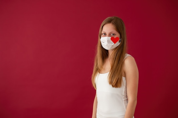 Solitary young Caucasian woman smiling under white face mask with red heart sign