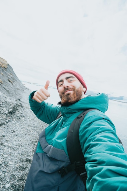 Solo male traveler on Iceland happy bout road trip new experiences Living freedom and explore backpacking Bearded hipster handsome guy doing the all good sign to camera taking a selfie while hiking